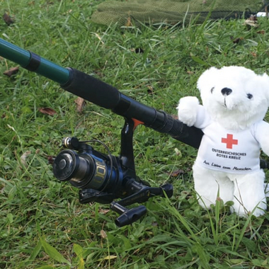 Bärli steht im Gras an einer Angel und wartet darauf, dass ein Fisch anbeißt - wie wir jetzt wissen wird er leider keinen fangen.