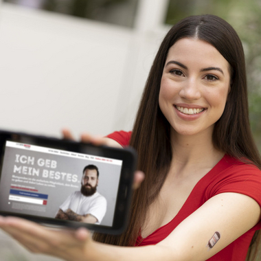 Auf dem Bild eine Dame sie hält ein Handy auf dem die Website gibt dein Bestes zu sehen ist