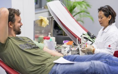 Ein junger Mann spendet sein Blut, eine Rotkreuz-Mitarbeiterin sitzt ihm gegenüber und kümmert sich um die erfolgreiche Blutsabnahme.