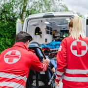 Eine Sanitäterin und ein Sanitäter schieben einen Patienten auf einer Trage in den Rettungswagen