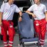 zwei Sanitäter stehen in Uniform links und rechts von einem Tragstuhl und vor einem Rettungsauto