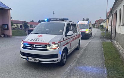 Ein Notarzteinsatzfahrzeug und ein Rettungstransportwagen im Einsatz auf einer Straße im ländlichen bewohnten Bereich.