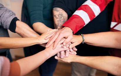 Mehrere Hände, die sich in der Mitte zusammentreffen; suggeriert Zusammenhalt