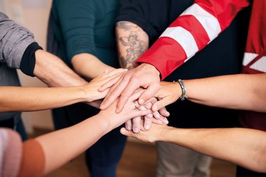 Mehrere Hände, die sich in der Mitte zusammentreffen; suggeriert Zusammenhalt