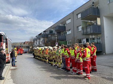Feuerwehrleute und Rotkreuz-Sanitäter:innen stehen gemeinsam vor dem Seniorenwohnhaus Hallwang