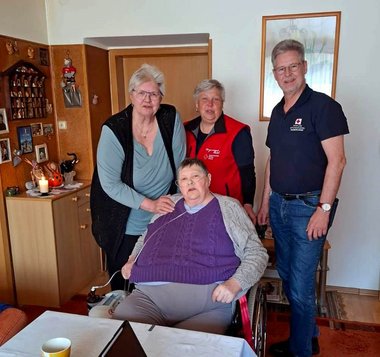 Eine Frau sitzt an einem Tisch, dahinter stehen drei Personen