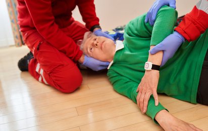 Eine Frau liegt am Fußboden und wird von Sanitätern versorgt.