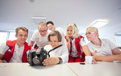 Freiwillige mit Blick auf die Kamera - © Österreichisches Rotes Kreuz (ÖRK) / Czech Freiwillige Mitarbeiter sitzen an einem Tisch und Blicken alle auf das rückwärtige Display einer Digitalkamera.