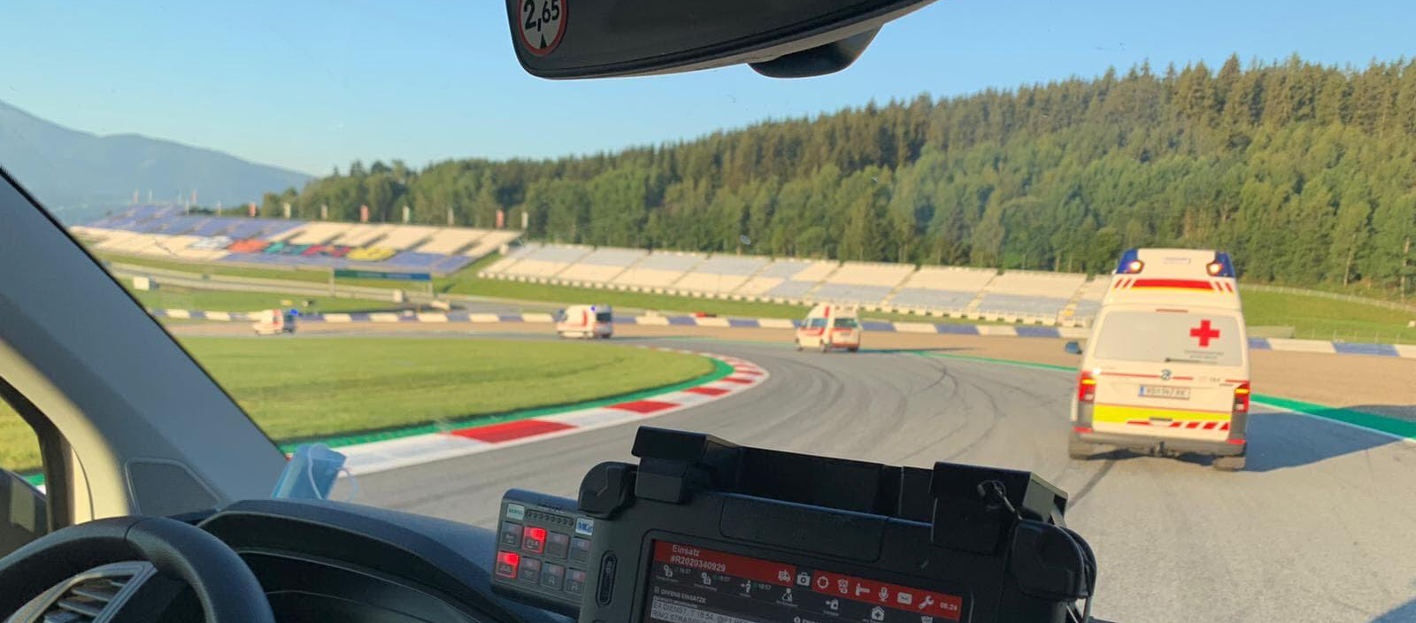 Formel 1 2020: Sujetbild - © Rotes Kreuz Voitsberg Einige Rettungswagen befinden sich auf einer Rennstrecke (dem Red Bull Ring) und beziehen grade ihre zugewiesenen Posten. Man sieht eine Fahrerkabine von Innen und weitere Rettungswagen vor dem Fahrzeug.