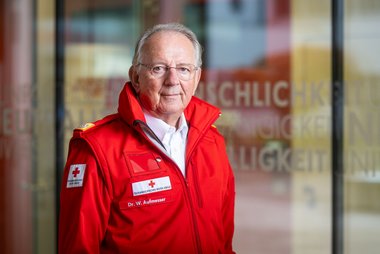 Porträtfoto von Doktor Werner Aufmesser, dem Präsidenten des Roten Kreuzes Salzburg, in einer roten Rotkreuz-Jacke.