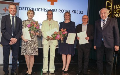 Sechs Personen stehen bei einer Veranstaltung des Österreichischen Roten Kreuzes auf einer Bühne. Drei Frauen und drei Männer halten Urkunden und Blumensträuße in den Händen.