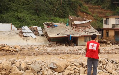 Rotkreuz Mitarbeiter vor durch Fluten zerstörtem Haus in Nepal