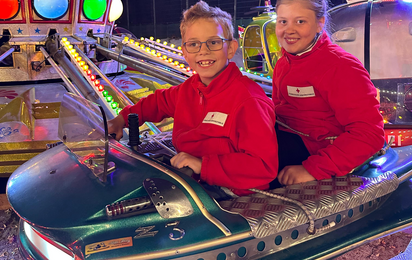 Zwei Jugendrotkreuz-Kinder sitzen glücklich in einem Ringelspiel.