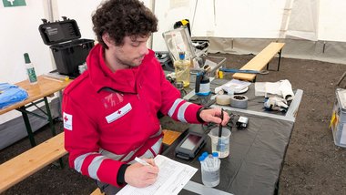 Ein Mann in Rotkreuz-Jacke analysiert eine Wasserprobe