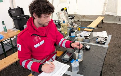 Ein Mann in Rotkreuz-Jacke analysiert eine Wasserprobe