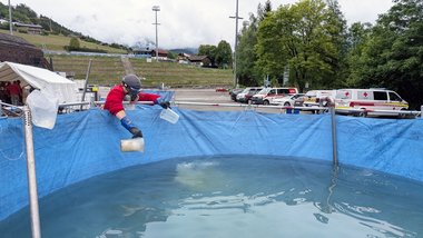 Ein Mann in Rotkreuz-Jacke und Atemschutz schöpft Wasser aus einem Becken