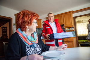 Eine Zuhause-Essen-Mitarbeiterin liefert eine Essenspaket an eine Klientin