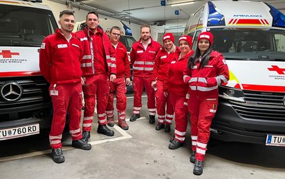 Mannschaftsbild in Rotkreuz-Garage, Sanitäter stehen zwischen zwei Rettungswagen.
