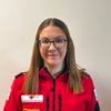 Jasmin Kober in weißem Rotkreuz-Polo vor unscharfem grauen Hintergrund.
