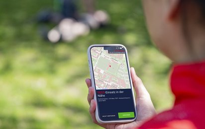 Eine Person hat ein Handy in der Hand und die Lebensretter:innen-App offen.