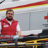 Manuel Rust steht neben einem Rettungswagen und reinigt die Fahrtrage mit einem Desinfektionstuch. Er trägt Uniform und hat Einmalhandschuhe an.