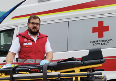 Manuel Rust steht neben einem Rettungswagen und reinigt die Fahrtrage mit einem Desinfektionstuch. Er trägt Uniform und hat Einmalhandschuhe an.