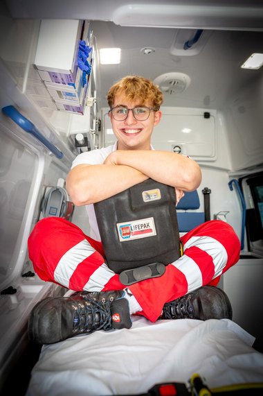 Zivildiener Alexander sitzt auf der Trage im Rettungsauto und hält einen Defibrillator in der Hand.