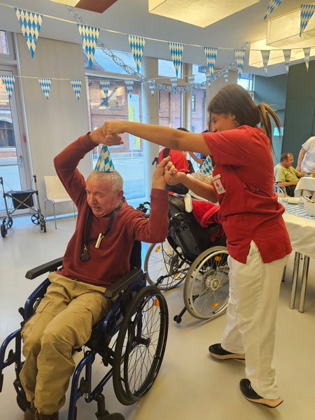Eine Pflegeperson tanzt mit einem im Rollstuhl sitzenden Herren.