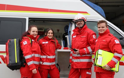 4 Rotkreuz-Sanitäter vor Rettungswagen