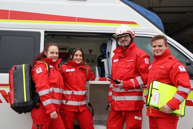 4 Rotkreuz-Sanitäter vor Rettungswagen