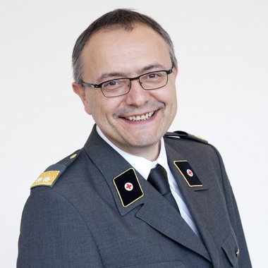 © STUDIOHORST Porträt eines lächelnden Mannes mit dunkler Brille in Ausgehuniform des Roten Kreuz Kärnten.