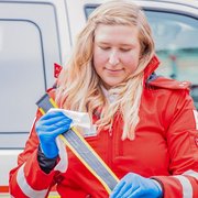 Freiwilliges Sozialjahr - © Rotes Kreuz Tirol ANDREAS AMPLATZ eine junge blonde Frau steht in Rotkreuz-Sanitäteruniform vor einer Trage und putzt die Gute der Trage