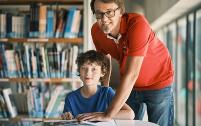 Ein Pädagoge in RK T-Shirt und ein Schüler in einer Bibliothek