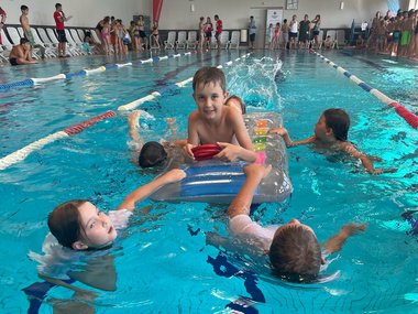Ein Schüler liegt auf einer Luftmatratze im Wasser und wird von anderen Schüler:innen am Wasser bewegt.