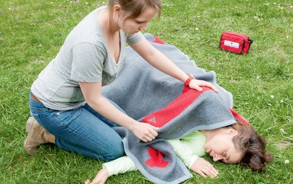 Eine Frau kümmert sich um eine Person die am Boden liegt.