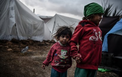Zwei kleine Kinder stehen Hand in Hand auf schlammigen Boden vor Zelten in Gaza.