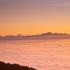 Man sieht einen wunderschönen Sonnenuntergang über einer Wolkendecke und Bergen im Hintergrund.