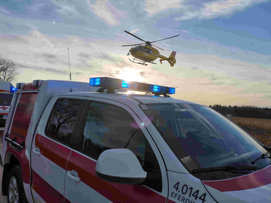 Notarztfahrzeug parkt, dahinter hebt ein Rettungshubschrauber ab
