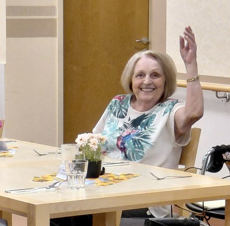 Eine Dame sitzt an einem Tisch und winkt
