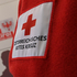 Zu sehen ist ein Teil einer roten Rotkreuz Fleecejacke mit dem Rotkreuz Logo. Im Hintergrund sieht man verschwommen das Logo des Landes Tirol