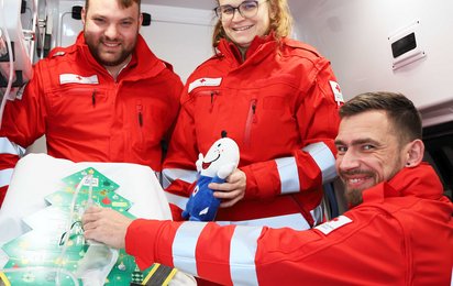 Drei Rettungssanitäter in Uniform mit Adventkalender im Rettungsauto