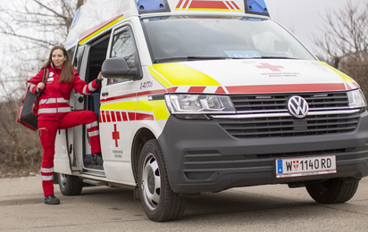 Eine junge Sanitäterin steht in der Tür eines Rettungsautos. Am Rücken trägt sie einen Notfallrucksack.