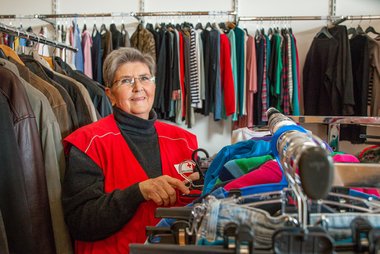 Eine Mitarbeiterin im Rotkreuz-Markt für Bekleidung steht zwischen den Kleiderständern auf denen die Ware präsentiert wird.