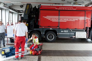 Rotkreuz-Sanitäter üben vor einem Feuerwehrfahrzeug die Versorgung einer verletzten Person