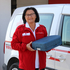 Eine Frau hält eine Essensbox in der Hand und steht vor einem Rotkreuz-Auto
