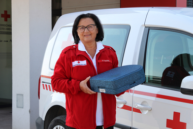 Essen auf Rädern - © OÖRK / Affenzeller Eine Frau hält eine Essensbox in der Hand und steht vor einem Rotkreuz-Auto