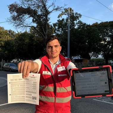 Ein D2D-Werber steht in Rotkreuz-Uniform und hält ein Mitgliederformular, sowie ein Tablet-PC in der Hand.