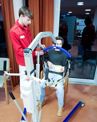 Ein junger Mann in roter Jacke bedient einen Hebekran, dahinter sitzt eine andere Person.