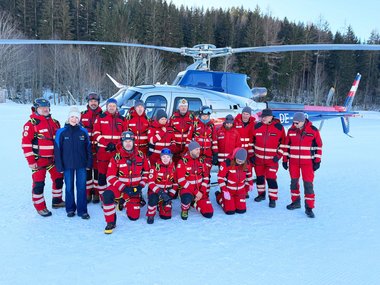 Das Team der Rotkreuz-Suchhundestaffel mit einer Vertreterin der Filzmooser Bergbahnen vor einem Hubschrauber.