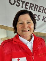 Waltraud Rauscher in roter Rotkreuz-Jacke vor einer Rotkreuz-Standarte.